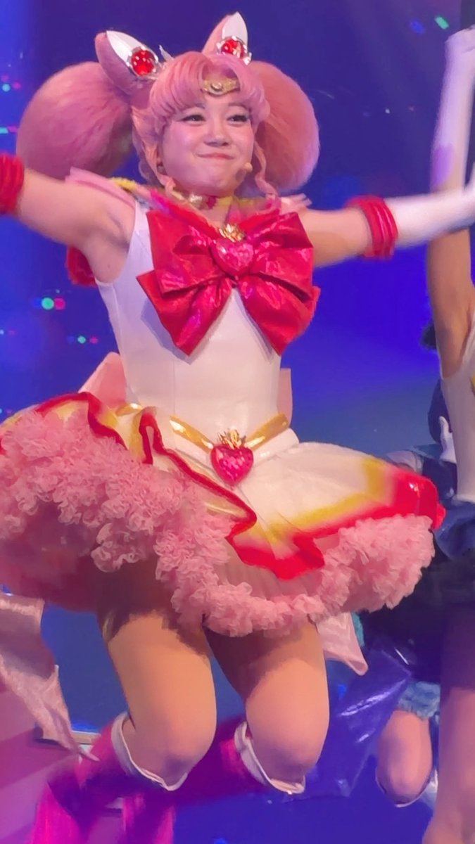 A performer in a Sailor Chibi Moon costume, complete with pink pigtails and a red heart brooch, dances on stage in a frilly red and white dress.