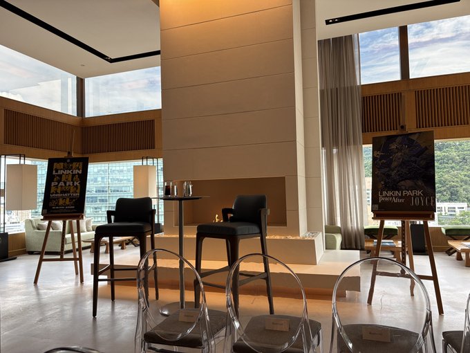 An elegantly set room featuring a 'LINKIN PARK From Zero World Tour' poster, along with signs advertising 'Joyce' and other sponsors, with high-back chairs and ghost chairs arranged for an event.