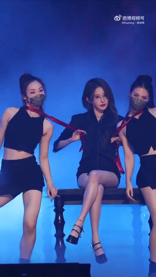A stage performance with three performers in black outfits and sparkly face masks, featuring one seated performer in the center holding red ties; Watson source on Weibo.