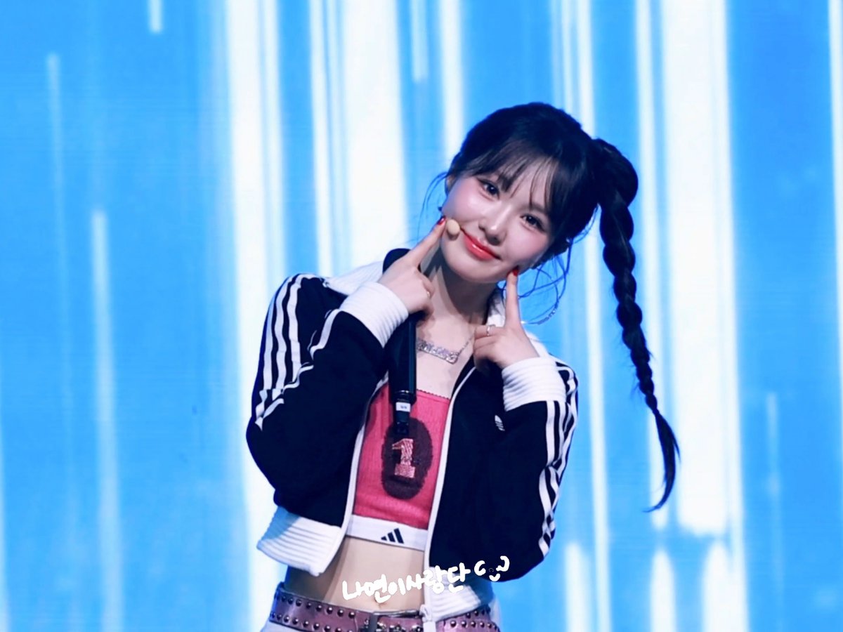 A K-pop idol with a long braided ponytail wearing an Adidas jacket and pink top, with Korean text '냉면이사랑다♡' visible at the bottom.