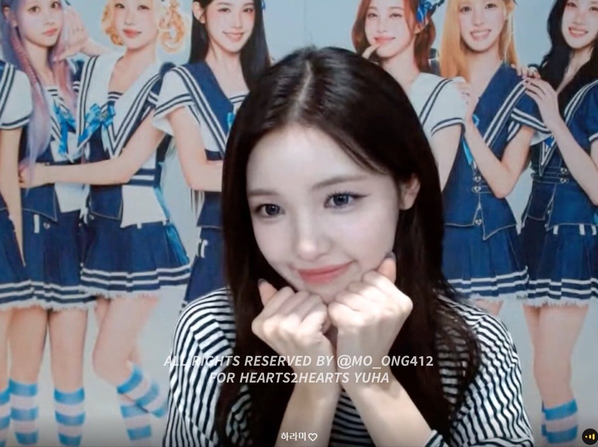 A young woman with long dark hair making a cute pose with her hands near her face, with an image of the K-pop group Hearts2Hearts in sailor outfits behind her and a watermark 'ALLRIGHTS RESERVED BY @MO_ONG412 FOR HEARTS2HEARTS YUHA'.