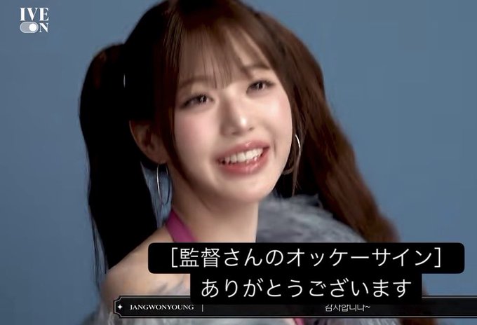 This image appears to be from IVE's "IVE ON" content, featuring member Jang Wonyoung smiling brightly in a behind-the-scenes moment, as she says "Thank you for the director's OK sign" (shown in the Japanese subtitles). The ASCII art in the accompanying post appears to be a playful decorative element unrelated to the image content itself.