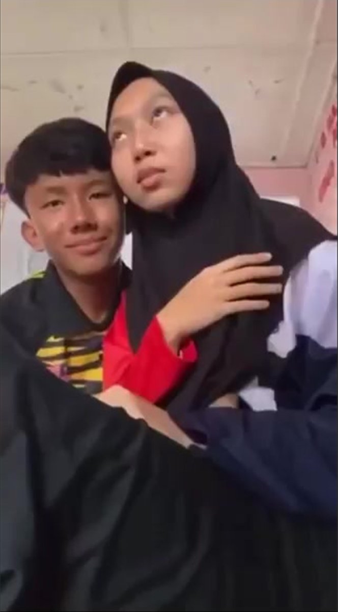 A young man in a dark jacket embraces a young woman wearing a black hijab and a red and white shirt, as they pose closely together with his arm around her. The image appears to be a casual, intimate couple's photo shared via the uc-share.com link, likely intended for friends to view or download.