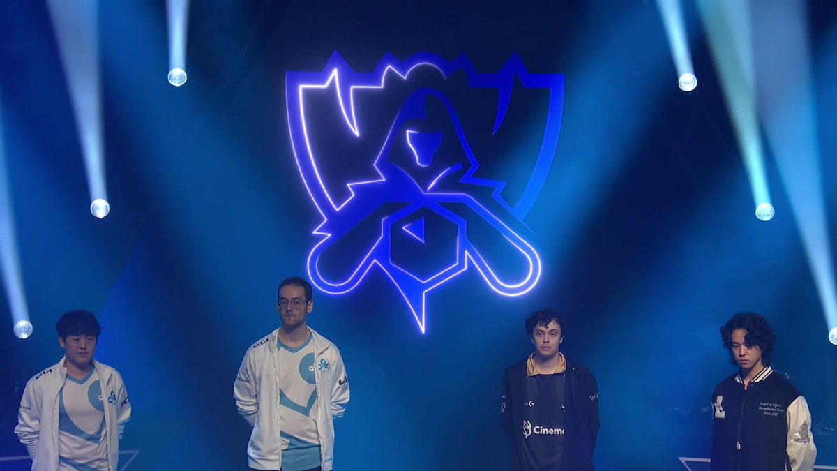 Four esports players stand on a stage beneath the illuminated logo of League of Legends team Rogue (the stylized hooded figure), with team apparel visible including sponsor logos like "Cinema." The atmospheric blue lighting and team lineup reinforce the post's theme of a championship journey, hinting at Worlds aspirations for Rogue.
