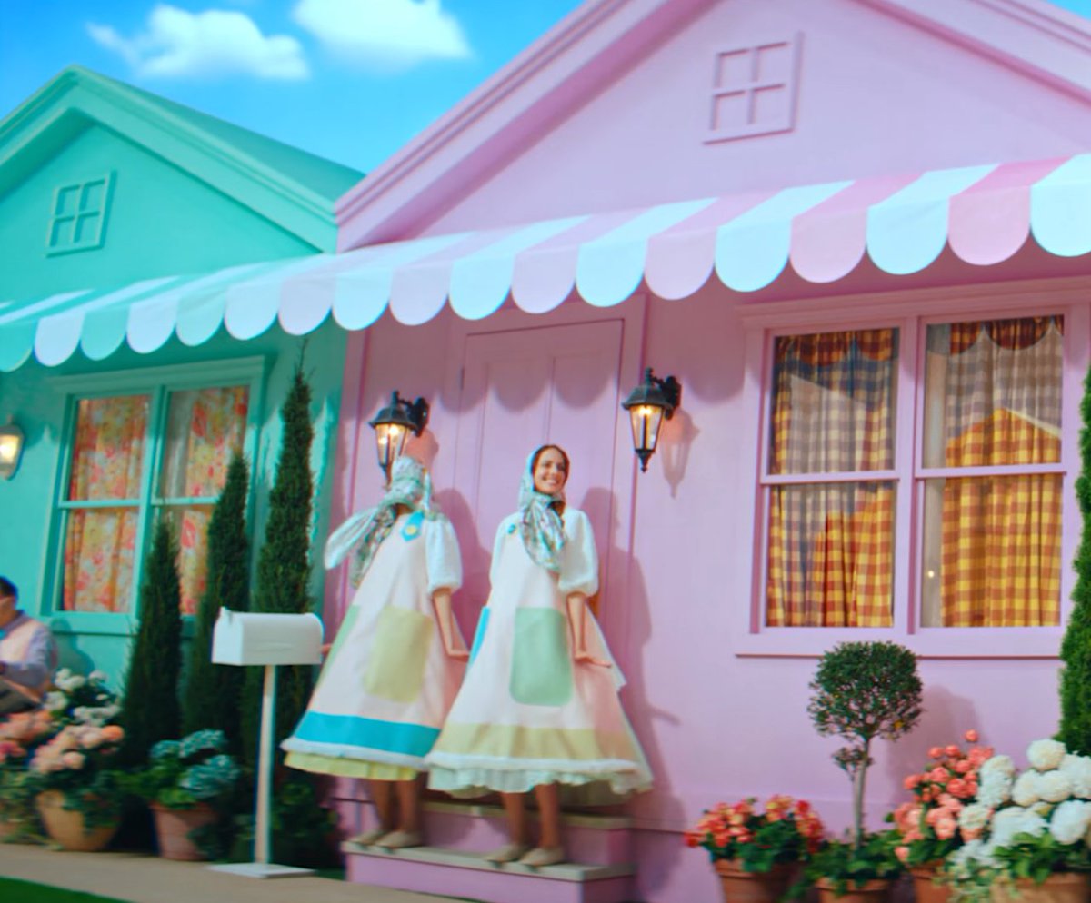 wattan5's tweet photo. #ミセスPOPS のMV #ミセス共犯 のMV考察です。
今までの #MrsGREENAPPLE の考察のようにMVの中の事実だけから考察していきます。
まず起床は起承転結の起。(@daystarter)さんかな？
おじさんが国際郵便を届けるのですが、間違っていたらごめんなさい。切手デザインが多分イラストレーター笠井由雅子さんかな？　と思いました。タッチが #金木和也 のジャケットデザインと似ていたので。
ではこの手紙は誰から届いたのでしょうか？「To dearest Mrs.GREENAPPLE」 と書かれています。
どこかアメリカのコメディドラマのような街。大森さんは 'A' と書かれた家から出てきます。　

何故'A'なのか違和感です。他の家にも棟なら表示されるはず。ＯやＭならまだしも。

そして「催し」でもあったまた新聞紙を持っている人がいます。
「催し」でも調べたらとんでもない事が書かれていましたが、今回も調べました。調べるの大変笑

 「More than a festival - a stronger Riverton」
（祭り以上のもの。リバートンを、もっと強い街へ）

という感じです。　ここまでなら違和感がないのですが、
その後の催しの掲示板に、

「A day filled with - good music, good food, great people and a FISH STORY or two.」
（良い音楽、おいしい食事、素晴らしい人たち、そして1つか2つの大袈裟な嘘に満ちた一日）

と、そんなこの明るい街を全否定し、しかも笑いながら後でハンマーで殴っています。やな世界。これも違和感。
違和感は続きます。　まず建物全体が、建物を色を左右対称に半分ずつ色を分けています。
シンメトリーというやつです。　また人間もシンメトリーに寄り添っています。
双子のように同じ動きをする２人がダンサー以外に６組も。
警官が分かりやすいですが、それ以外にもめちゃくちゃいます。

なのにシンメトリーではない人達もいます。　それは Mrs.GREENAPPLEです。
他にもいますがそれは後ほど。

「共犯」の歌詞を見ればみるほど、聴けば聴くほどこの歌詞とメロディに合うのは、
それこそ「ア・ポステリオリ」のようなＭＶが似合いそう。
それをあえてメロディもＭＶも見た目をPOPSに仕上げきっているのは狂気すら感じます。
ただ、MVは狂気じみた違和感がたくさんあるということ。
それをただ目を瞑って過ごしているのなら、
誰もが共犯だと思う。
大森さんと馬をかついでいる郵便配達員のおじさんは、大森さんが見ていない時だけ苦しそうにしている。
大森さんが振り返ったら愛想笑いをし、また顔が戻ったらまた疲れている。

知ってて知らないふりしている世界
シンメトリーだと思っていたのは、アシンメトリーの世界

それは別に大森さんだけじゃない。
この世界が突然終わり、次は同じ演者が同じ自分を見ているアシンメトリーの世界観に変わります。

観客の後ろには 'STAGE B' と書かれています。

これだけじゃ違和感はないですが、大森さんは 'A' から出てきました。
無関心にただ見ていた大森さんですが、

「素晴らしさを分かってはいるのに　この世界に生まれたらもう共犯」

と口ずさみ立ち上がる。次に若井さん藤澤さんが立ち上がり、次に１人だけステージでもステージ外でも同じ服の女の子が共感する。
共犯という名のアシンメトリーな自分自身を’共生’として受け入れたのだと思います。
それがMrs.GREENAPPLEの大森元貴だとしても、というか「GOOD DAY」という楽曲をフェーズ３の頭にリリースしたのも
色々な事を腹をくくったのかな？　二人も。そうしたのもそうなったのも自分自身だけど、
僕も二人も、もう腹をくくったから、聴いている貴方たちも共犯なんですよと。

ならMVの最初に戻って、「To dearest Mrs.GREENAPPLE」は誰なのでしょうか？

JAM'S。

部屋から出ていく時、大森さんは手紙を見てうなずいている。わかった。わかってる。
最後にはこのアシンメトリーな世界を見ていたのは、様々な色も形も異なる宇宙人で、共感しています。

ただ、そのＵＦＯの室内には、全く意味のない 'C' と書かれています。

内から外へ出て行ってる。なら、'D'は？

実際には 'D' はあります。
それはこのMVを観てしまった外の世界の私たちです。
もう観てしまったからには、考察してしまったからには、もう共犯なんです。

最後に。

違和感のサラリーマン風男性がずっと背中に青い張り紙を15枚ほどつけて歩いています。
本人は知らなさそうなのですが、左右ずっと歩いて本人以外はみんな気づいています。

映画「バックトゥザフューチャー」でもあった「Kick Me!（蹴って！）」といういたずらかもしれません。
これに気づいたのはＡＢＣＤ全員なのに、あれだけわかりやすく見てるのに誰も背中の張り紙について話さない。

あんまり考えたくはないですが、もし本当に「Kick ME」なら、
いじめられているのに、手を差し伸べないのなら、それはもう貴方も共犯です。

MVでは、貼られているサラリーマンが、おばあさんに挨拶し、
おばあさんだけが気づいて張り紙を１枚はがしている。
よく見ると、おばあさんは驚いた場面もあります。

剥がした１枚をポストに貼り付けています。　その１枚はハンマーで叩いている若井さんの後ろのポストに。
ボケていますが、文字からいってあの言葉かもしれません。忘れないための「餅つき大会」とかのメモならいいな。

８番出口のように、困っている人がいたら、助けを求めている人がいたら見ぬフリはやめようねっていう。
言葉は毒にも薬にもなるけれど、薬だけ持ち歩きたいな。
アシンメトリーな自分自身にも共生して生きていく。
ただ、優しさも分け合ってこそ、見事に共犯です。

ミセスと共に共生して、運命共同体。素敵な共犯になりましょう。

以上、共犯考察でした！👀👀