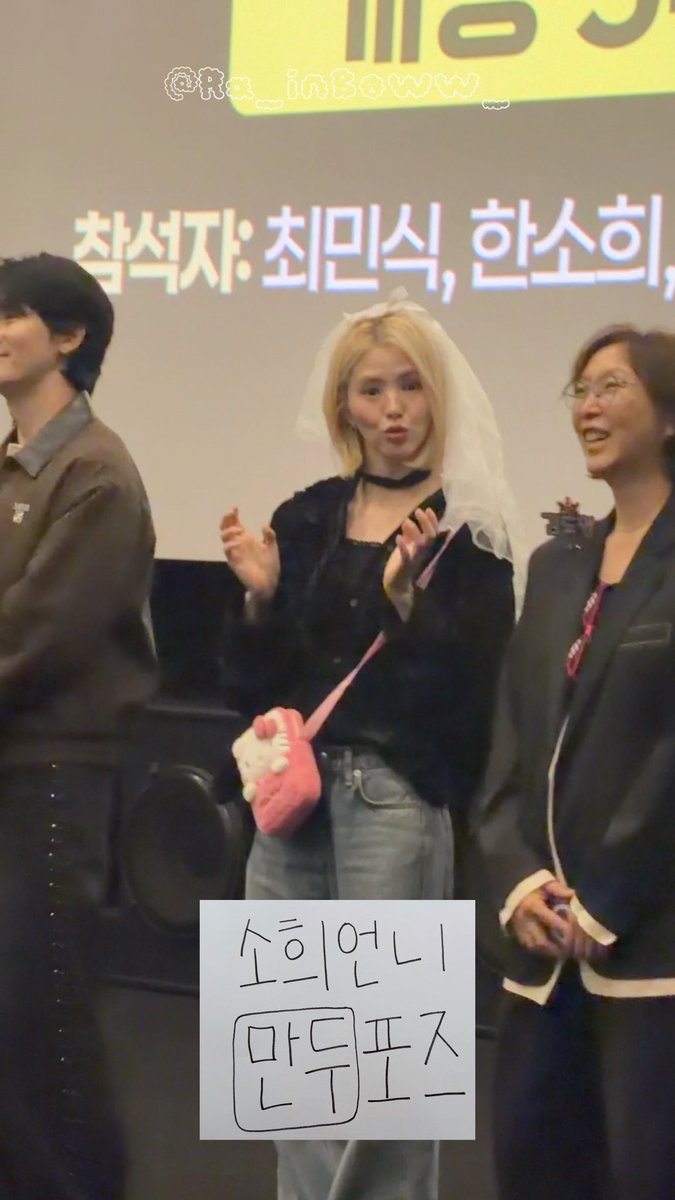 A fan takes a mirror selfie at a Korean event, with a handwritten Korean sign referencing soprano and madpuffs, while a screen in the background displays Korean credits.
