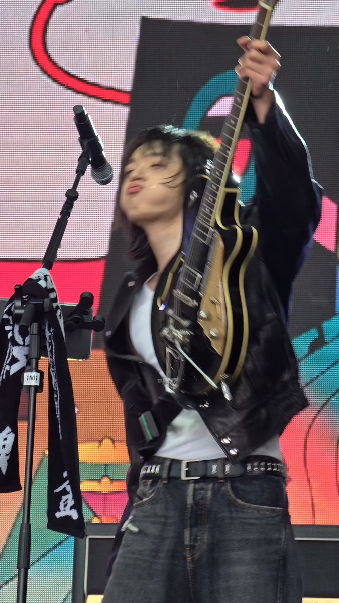 A musician on stage passionately playing an electric guitar while wearing a leather jacket, captured mid-performance with hair flying.