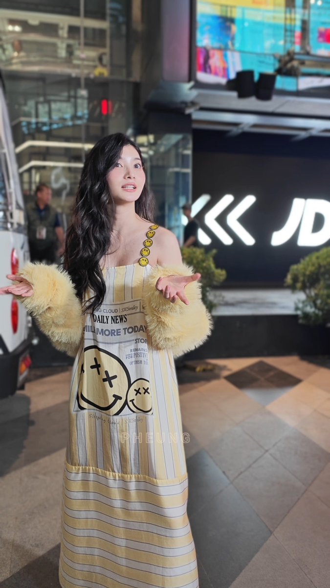 A woman stands outdoors at night wearing a yellow and white striped strapless dress with yellow fur sleeves and smiley face buttons; the watermark "PHEUNG" appears across the image.