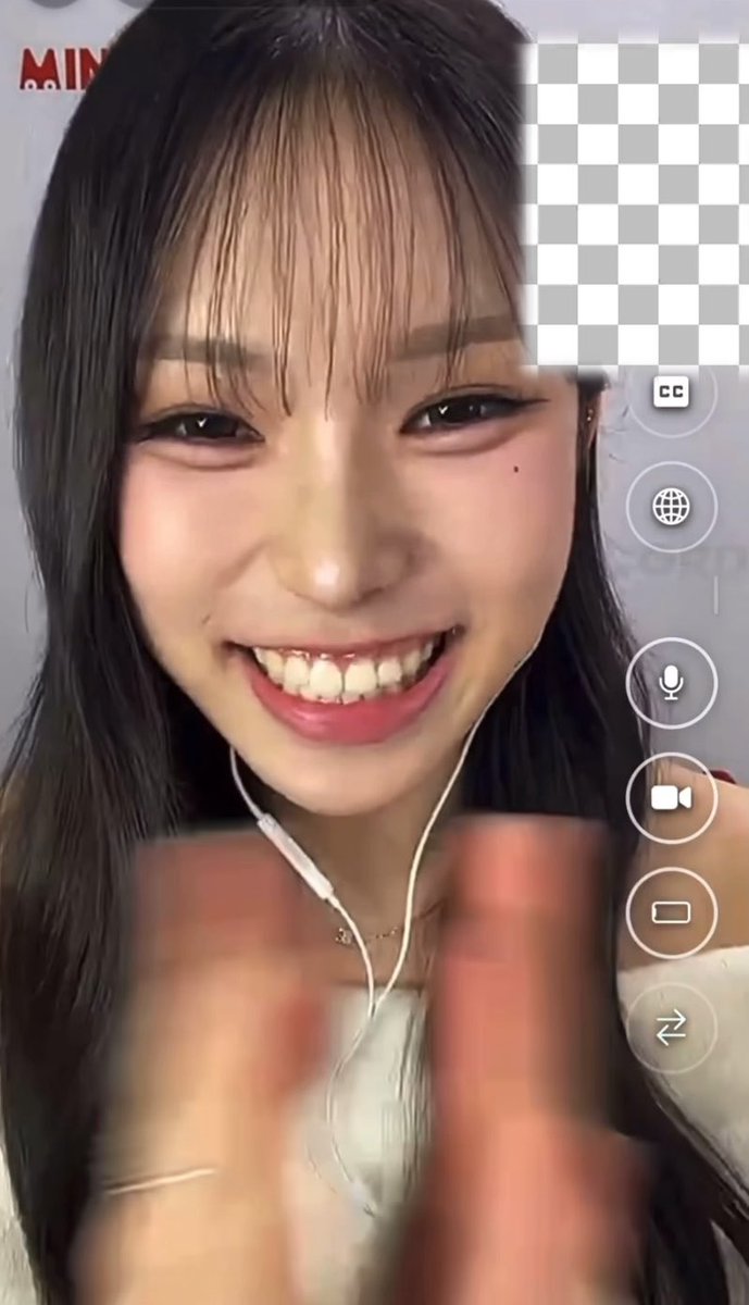 A screenshot from a video call featuring a smiling young woman with long dark hair and wired earphones, with a blurred hand visible in the foreground. The video interface icons (microphone, camera, etc.) appear on the right side, while the post text suggests this is a reaction she's making to something with such high energy it would cause someone to faint upon learning what prompted it.