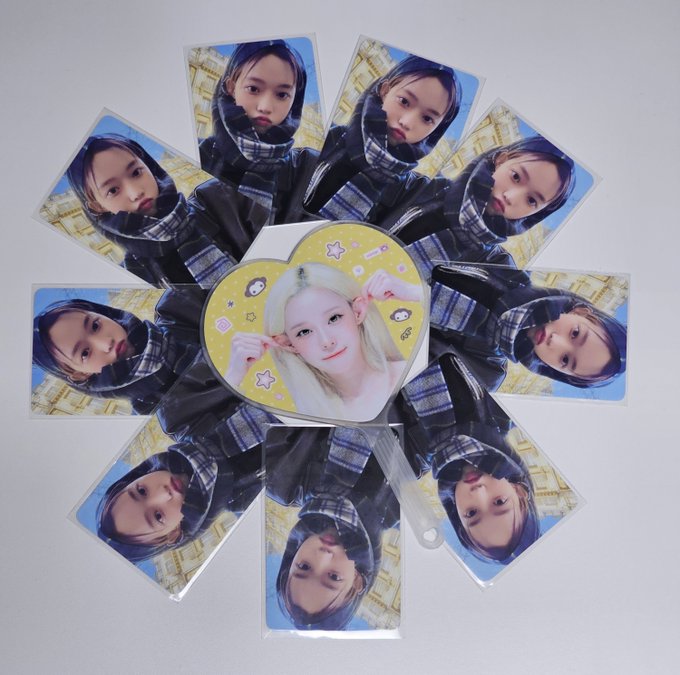 K-pop photocards are arranged in a circular fan pattern featuring a blonde woman in the center heart shape and repeated images of another member in black around it.