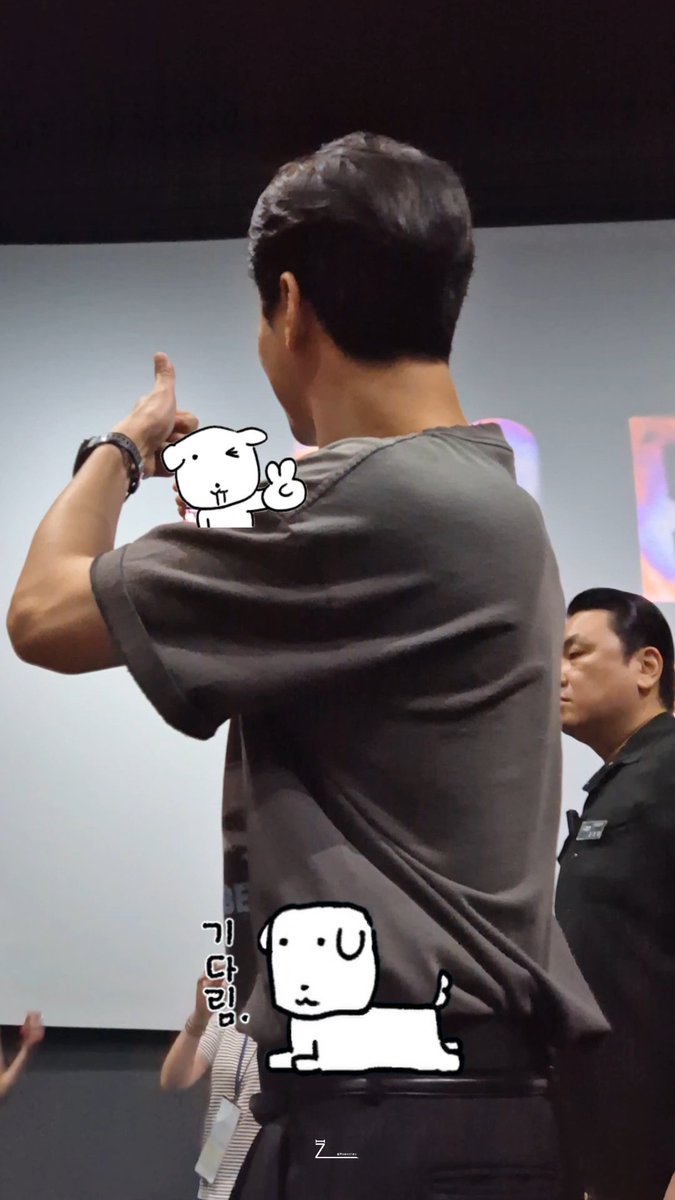 Man in gray t-shirt at event with cartoon stickers on image and Korean text '가다님다'