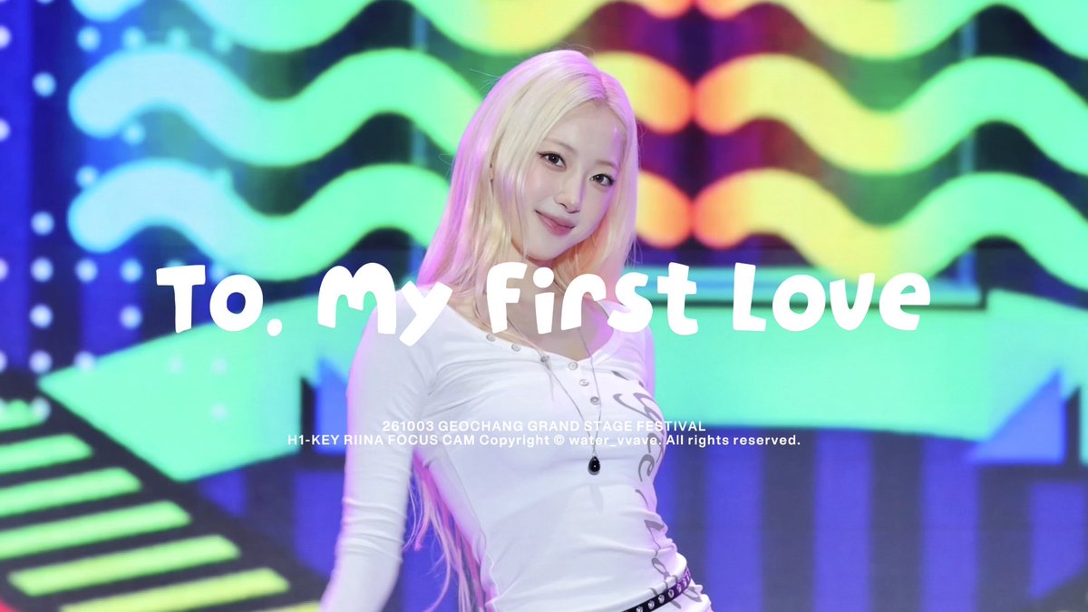 A K-pop performance photo of H1-KEY member Riina with blonde hair at the 261003 Geochang Grand Stage Festival, with the text 'To, My First Love' overlaid, credited to water_vvave.