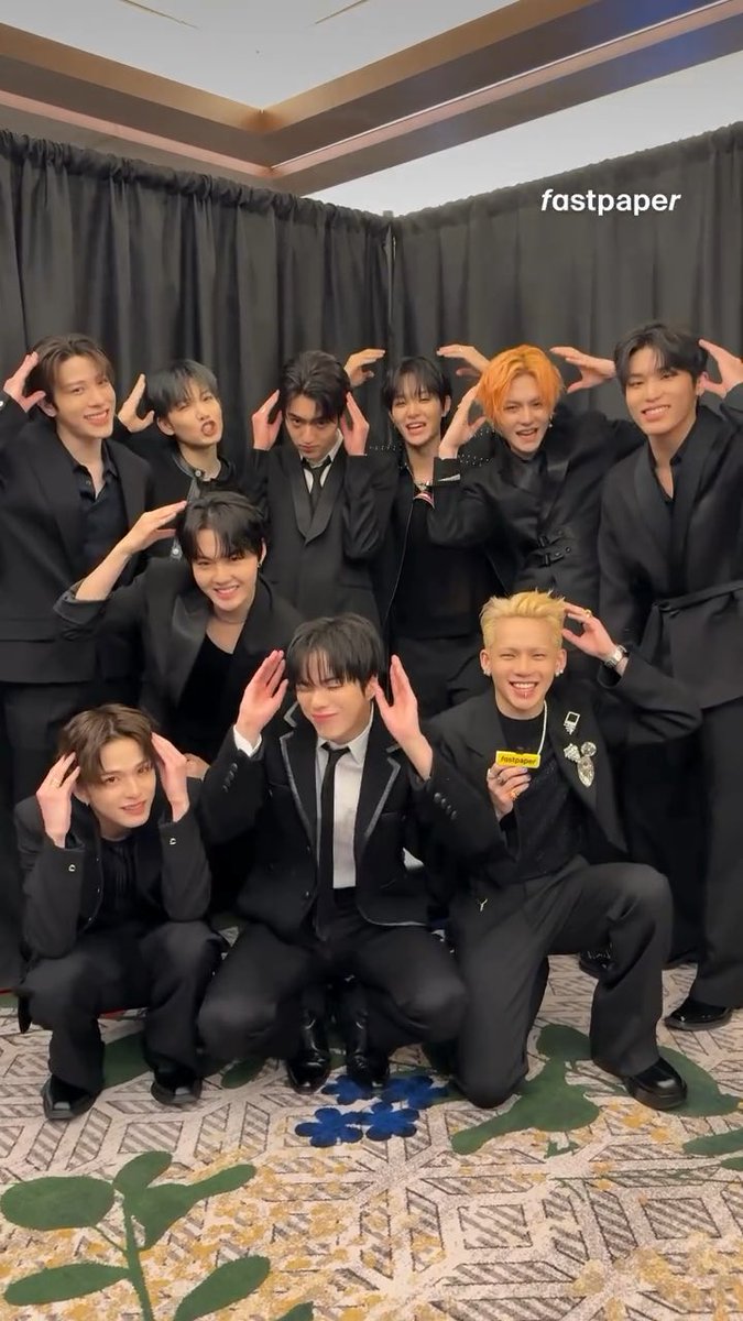A group of ten men in black suits pose together, holding their hands up by their heads to make bunny ears.