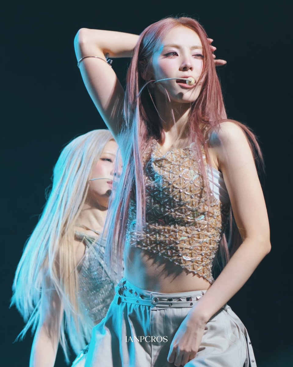 A concert photograph showing a female performer with pink hair wearing a bedazzled top and headset mic, with the watermark 'IANPCROS' at the bottom.