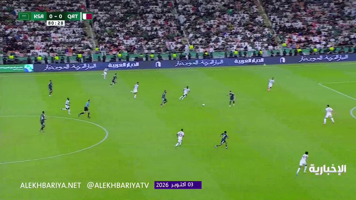 A wide-angle shot captures a tense moment during the Saudi Arabia vs. Qatar match (KSA 0-0 QAT) at the 80:28 mark of the 27th Gulf Cup, as the Qatari goalkeeper rushes out to block a shot from Firas Al-Buraikan near the edge of the penalty area, with Al-Ekhbariya TV graphics visible on screen.
