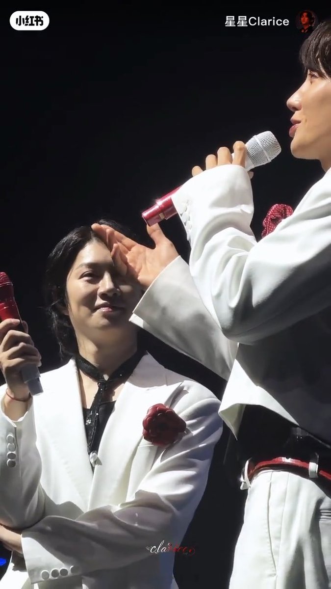 Photo from Xiaohongshu (小红书) by user '星星Clarice' showing two men in white outfits performing on stage; the man on the left is shielding his eyes while the other holds a microphone. Watermark reads 'claricco'.