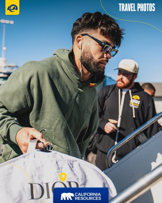 A bearded man wearing sunglasses, a green hoodie, and earbuds disembarks from an aircraft carrying a white "DIOR" duffle bag, while a man in a white cap and black Rams hoodie waits nearby. The graphic overlays feature "TRAVEL PHOTOS," a Los Angeles Rams logo, and a "California Resources" banner with a location pin, tying into the #RamsHouse travel theme sponsored by California Resources Corp.