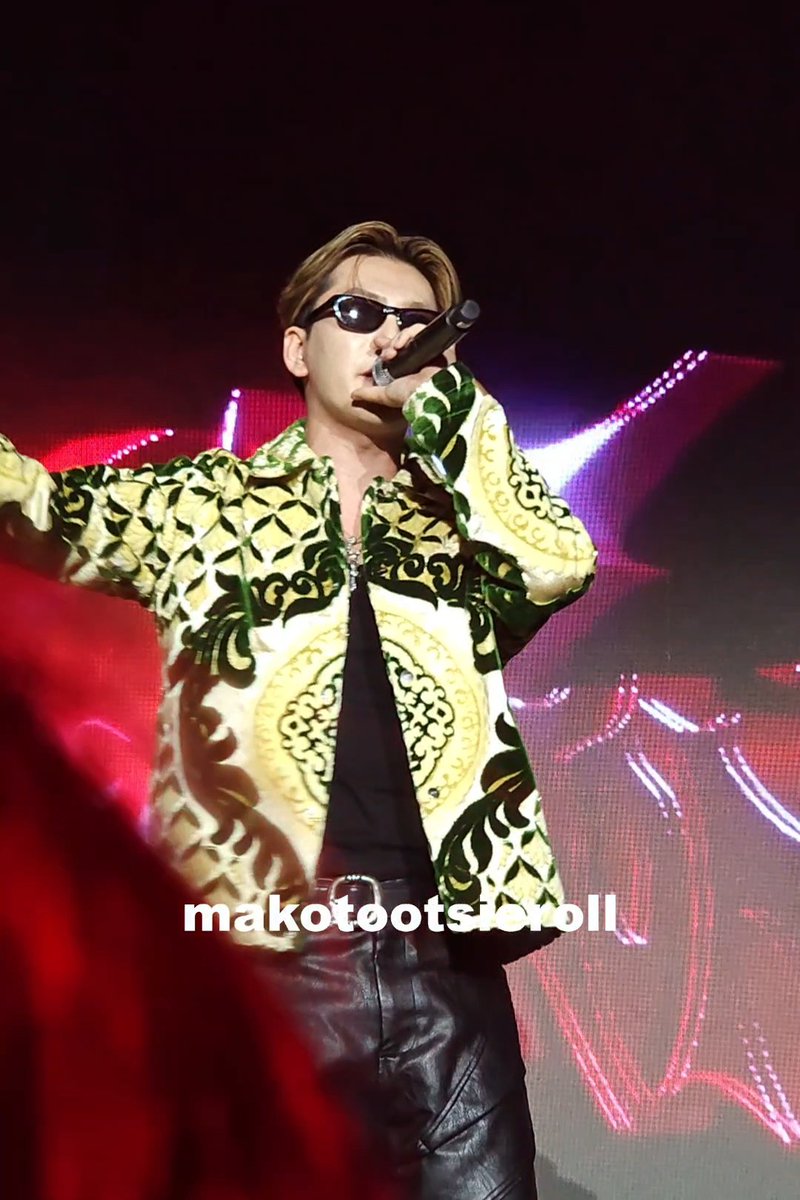A performer on stage wearing sunglasses and an ornate green and gold patterned shirt sings into a microphone, with the watermark "makotootsiskroll" displayed across the image.