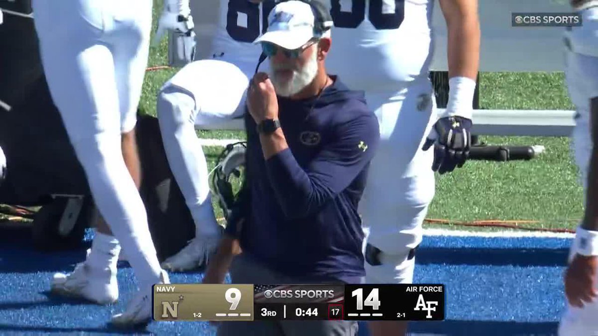 A coach wearing a navy Georgia Tech hoodie and white cap looks on with a concerned expression, pressing his hand to his headset during a Navy vs. Air Force game shown on CBS Sports, with the scoreboard displaying Air Force leading Navy 14-9 with 44 seconds left in the 3rd quarter, capturing the tense moment following a fumble.