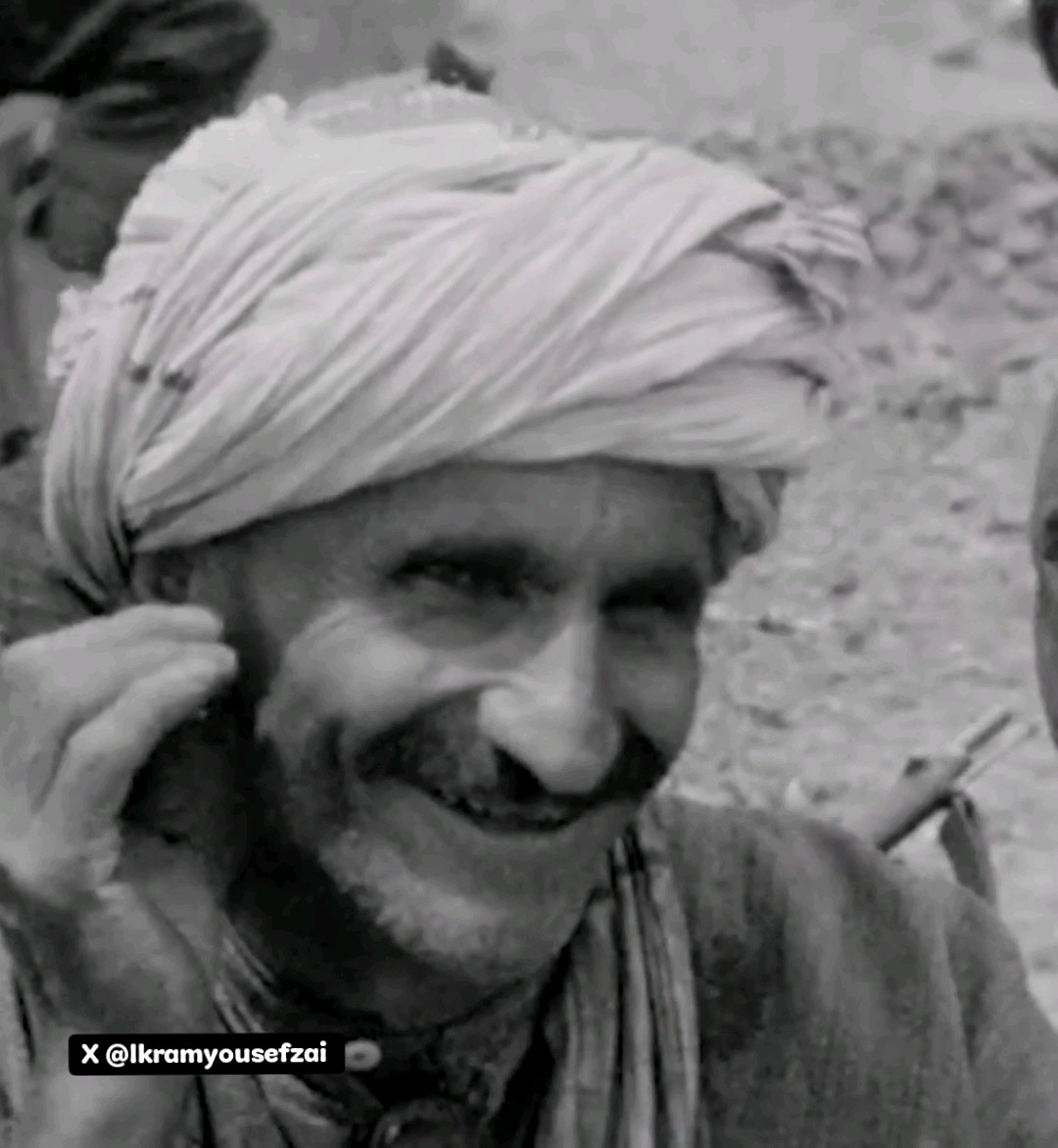 A smiling man with a thick mustache wears a traditional white turban in this vintage black-and-white photograph capturing a candid moment from 1928 Peshawar, NWFP. The watermark "@lkramyousefzai" appears in the bottom left corner, likely crediting the X/Twitter user who shared this historical glimpse into the region's past.
