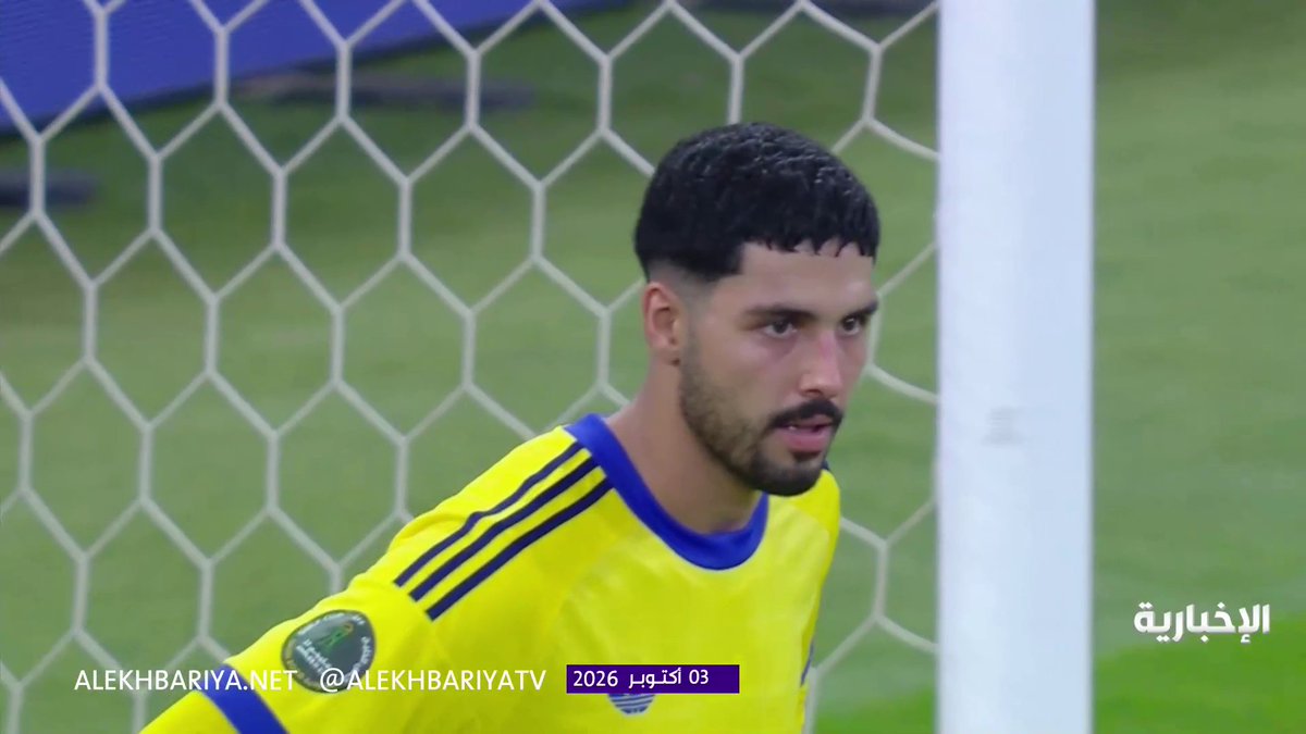 A Saudi Arabian goalkeeper in a yellow and blue jersey stands in front of the goal net following his team's penalty shootout victory over Qatar in the #Khaleeji_27 championship semifinal. The image includes the watermark "ALEKHBARIYA.NET @ALEKHBARIYATV" and a date stamp reading "03 أكتوبر 2026" (October 3, 2026), with the Arabic text "الإخبارية" (Al-Ekhbariya) visible in the corner.