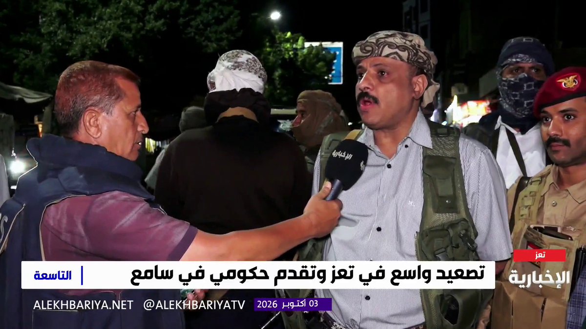 A news broadcast screenshot from Al Ekhbariya showing an interview at night with a man in a striped shirt and tactical vest, with Arabic text at the bottom including '03 أكتوبر 2026' and @ALEKHBARIYATV.