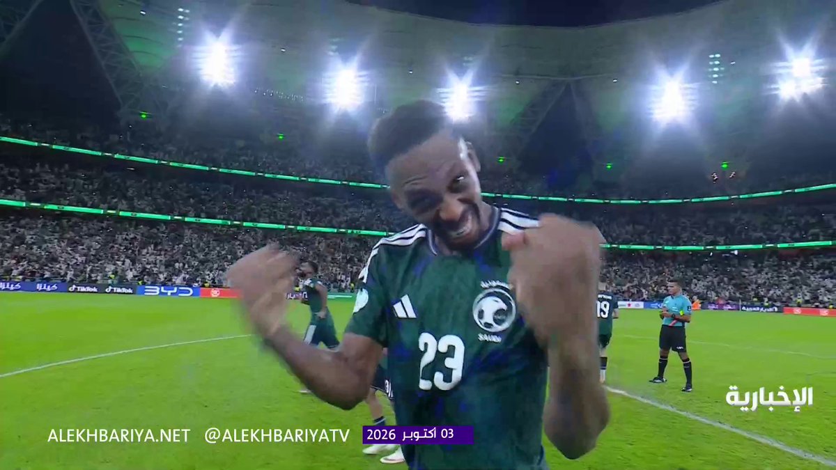 A jubilant Saudi Arabian national team player, wearing the green #23 jersey, celebrates with a clenched fist and big smile in a packed stadium after his team secured a place in the Gulf Cup 27 (Gulf 27) final. The scene is broadcast by Alekhbariya (@ALEKHBARIYATV) with the timestamp "03 أكتوبر 2026" (October 3, 2026), capturing the players' excitement following their qualification.