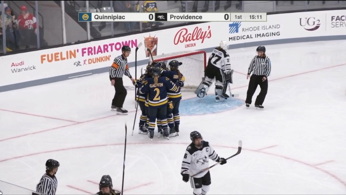 Quinnipiac women's hockey players (#2 Gaudin and teammates) celebrate a goal against Providence at 15:11 in the 1st period, with the game tied 0-0 on the scoreboard at the start of the clip. The celebration near the Providence goaltender (#37) captures the moment just after the first goal was scored in this NCAA matchup broadcast on ESPN+.