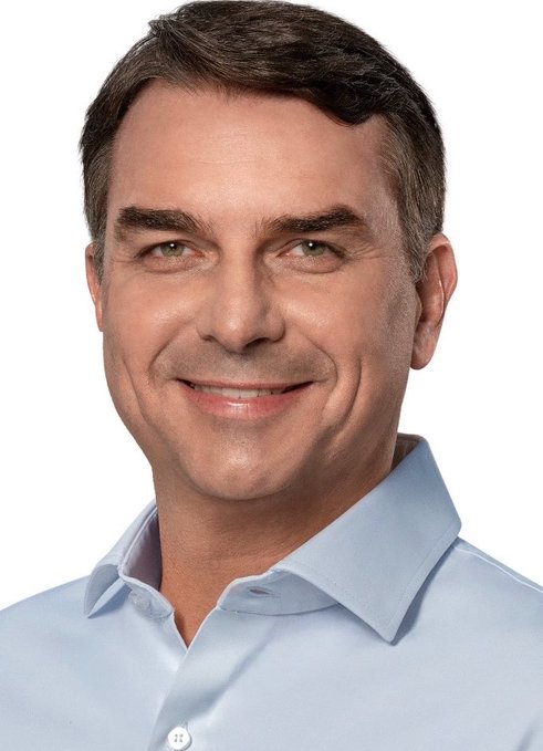 A headshot of a smiling middle-aged man with dark hair wearing a light blue button-up shirt appears alongside polling data showing Flávio Bolsonaro (PL) leading with 47% support against Lula's 43% in a national Brazilian presidential race survey.