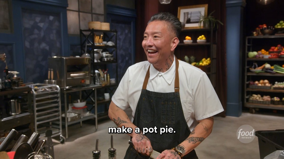 A smiling man with tattoos wearing a white shirt and dark apron stands in a kitchen setting, with a Food Network logo and the subtitle 'make a pot pie.' visible.
