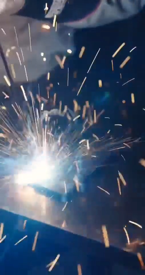 Bright welding or grinding sparks spray outward against a dark, blue-toned background.