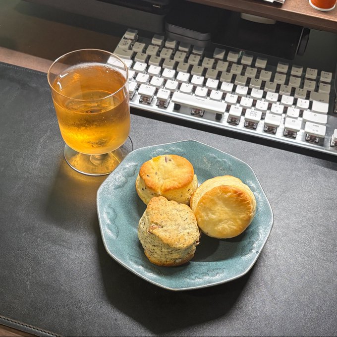 A top-down view of a teal plate holding three scones next to a glass of iced tea, set on a desk with a mechanical keyboard in the background.
