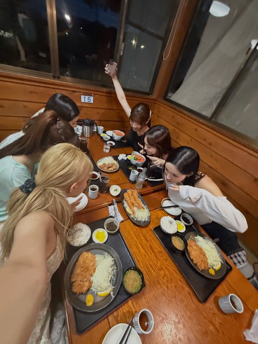 A group of women enjoy a meal together at a wooden table in a restaurant, featuring trays of tonkatsu (breaded cutlets) with shredded cabbage, lemon wedges, rice, and miso soup.