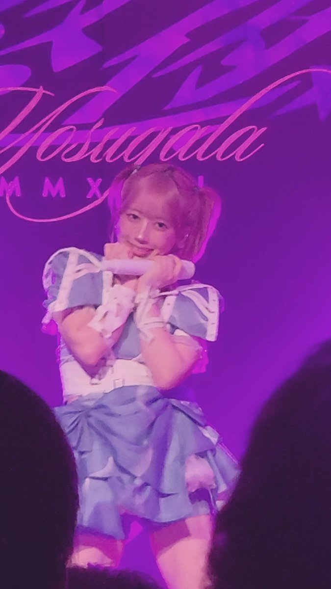 A performer on stage in a blue and white ruffled outfit poses under purple lighting in front of a backdrop reading 'Jashud' and 'MMX'.