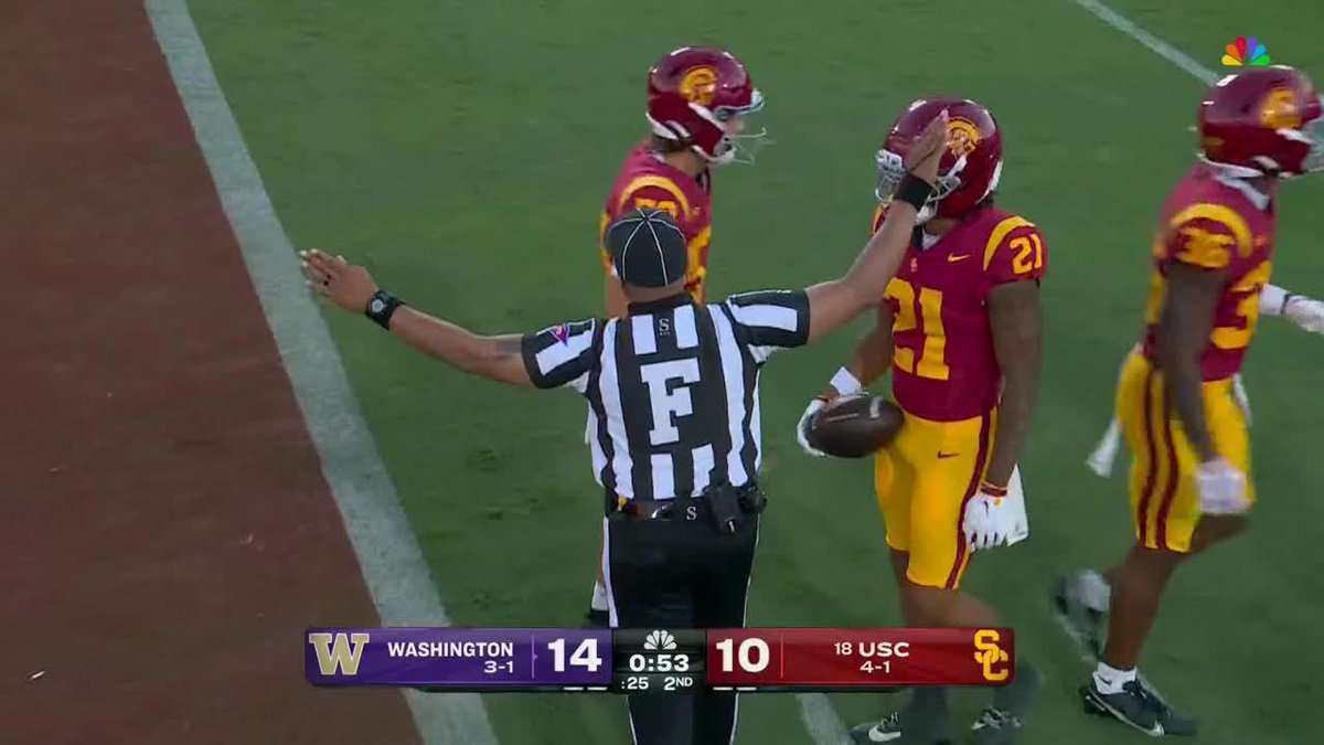 A referee signals a stoppage in play as USC players in cardinal and gold uniforms celebrate a well-placed punt near the goal line, with the scoreboard showing Washington leading USC 14-10 with 0:53 remaining in the 2nd quarter. The image captures the moment after the punt was downed at the one-yard line, pinning Washington deep in their own territory.