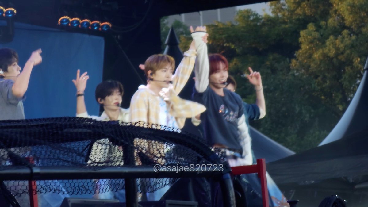 Young performers on an outdoor stage wave to the crowd, with a watermark reading '@asajae820723' visible at the bottom of the photo.