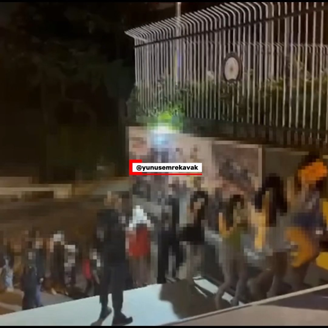 A blurry, low-light photograph of a crowd of people standing outside at night, with a watermark reading '@yunusemrekavak'.