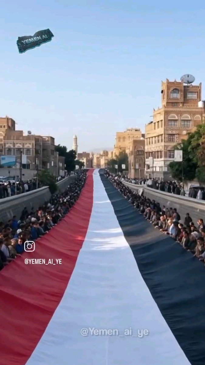A massive Yemeni flag (red, white, and black stripes) being held up by crowds lining both sides of a street, with '@YEMEN_AI_YE' and 'YEMEN AI' text overlays visible.