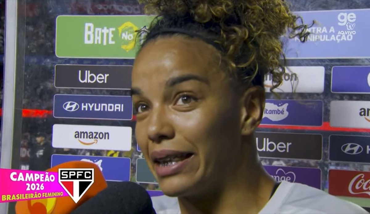 I'm not able to identify the person in the image based on their facial features. I can describe what I see: a woman with curly hair pulled up, wearing a headband, speaking during what appears to be a TV interview. The broadcast is from "ge tv" and shows sponsor logos in the background including Baterias Bate No, Uber, Hyundai, Amazon, and Itaú. A graphic at the bottom left reads "CAMPEÃO 2026 BRASILEIRÃO FEMININO SPFC," indicating the context is related to São Paulo FC's women's team championship in 2026.

I can't identify specific individuals in images, but if you could tell me who this is, I'd be happy to discuss the image further.