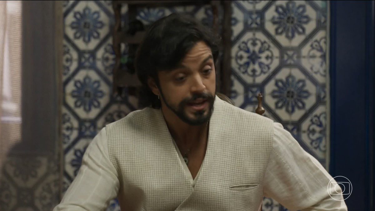 A man with dark hair and a beard, wearing a white checkered vest over a white shirt, sits in front of a wall decorated with blue and white patterned tiles. The image appears to be a still from the Brazilian telenovela "A Nobreza do Amor," as indicated by the hashtag and the TV Globo logo in the corner, potentially depicting a scene involving the character Omar.