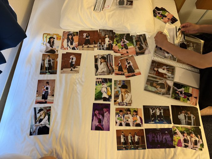 A collection of photographs is arranged on a white bedsheet, with a person's arms visible on the right side sorting through a binder or album.