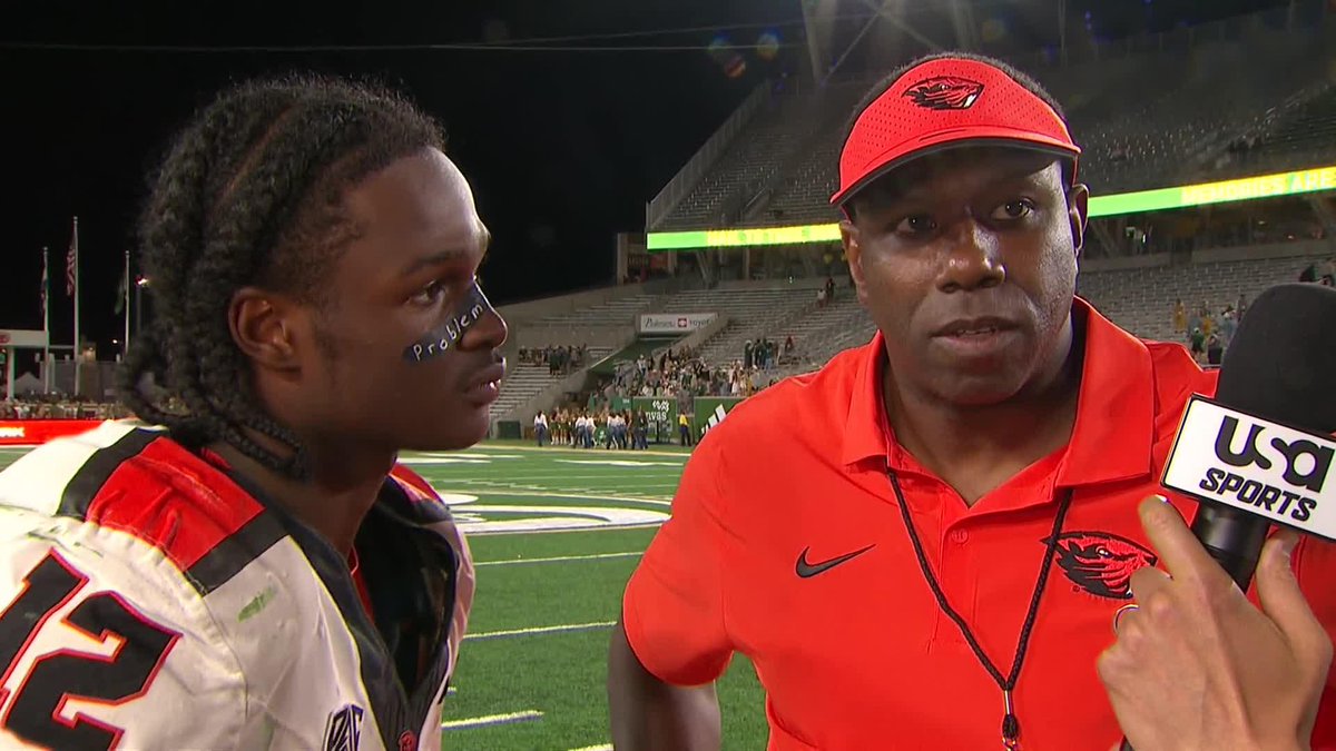 A post-game interview on a football field features a coach in a red Oregon State cap and polo alongside a player with eye black reading "PRODUCTIO" and the number 2 on his jersey, as a USA Sports microphone is held up to them. The image captures Coach Shepard's post-game remarks about his team's potential following their dominant conference victory, with the stadium and remaining crowd visible in the background.