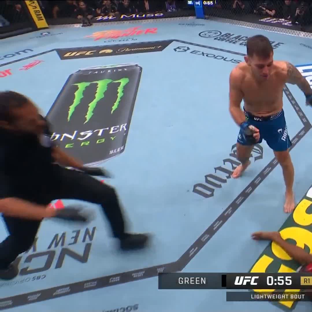 The caption should describe a UFC fight scene where a fighter in blue shorts stands in the octagon after apparently finishing his opponent quickly. Key text visible includes "GREEN," "UFC 0:55 R1," "LIGHTWEIGHT BOUT," along with sponsor logos like "Monster Energy," "Paramount+," "Exodus," and "Devour."

**Caption:** A UFC lightweight bout shows fighter Green in blue shorts standing over his downed rival in the octagon with 0:55 left in Round 1, following a rapid finish.