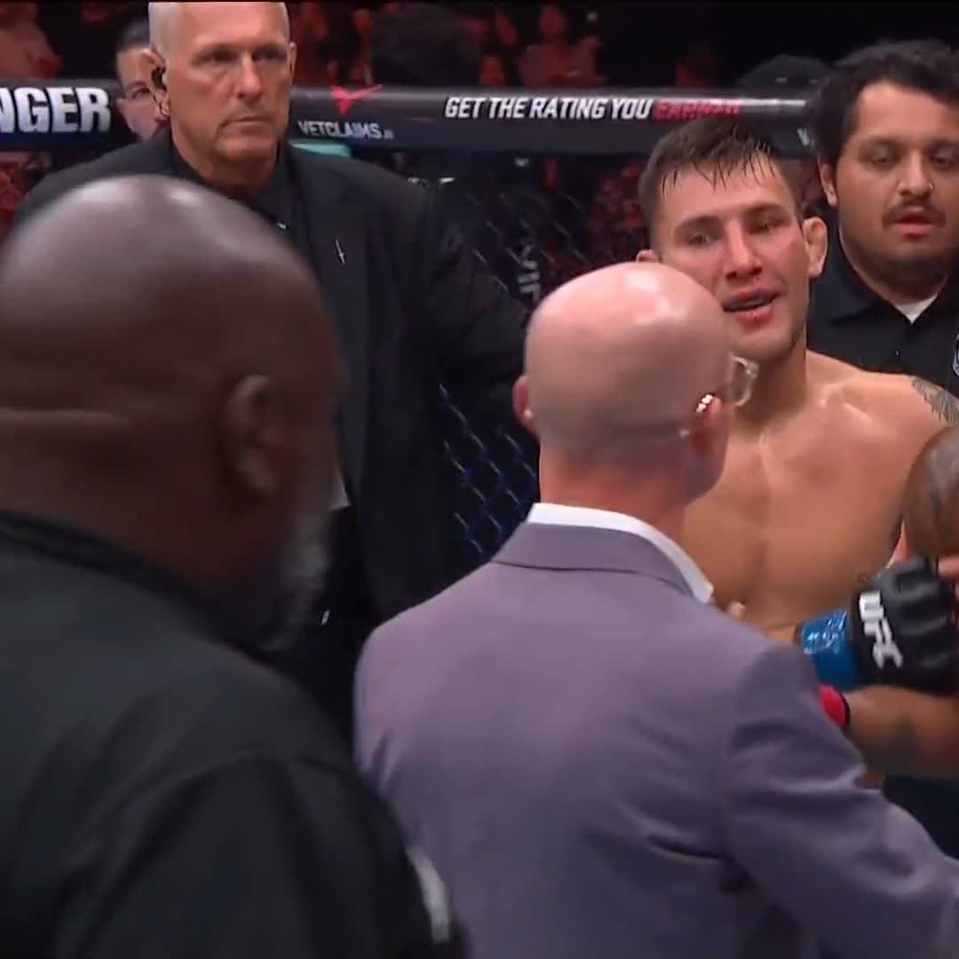 Esteban Ribovics, shirtless and visibly emotional, stands in the UFC octagon surrounded by officials and cornermen following his first-round knockout victory, with "GET THE RATING YOU" and "VETCLAIMS" advertisements visible on the cage behind him.