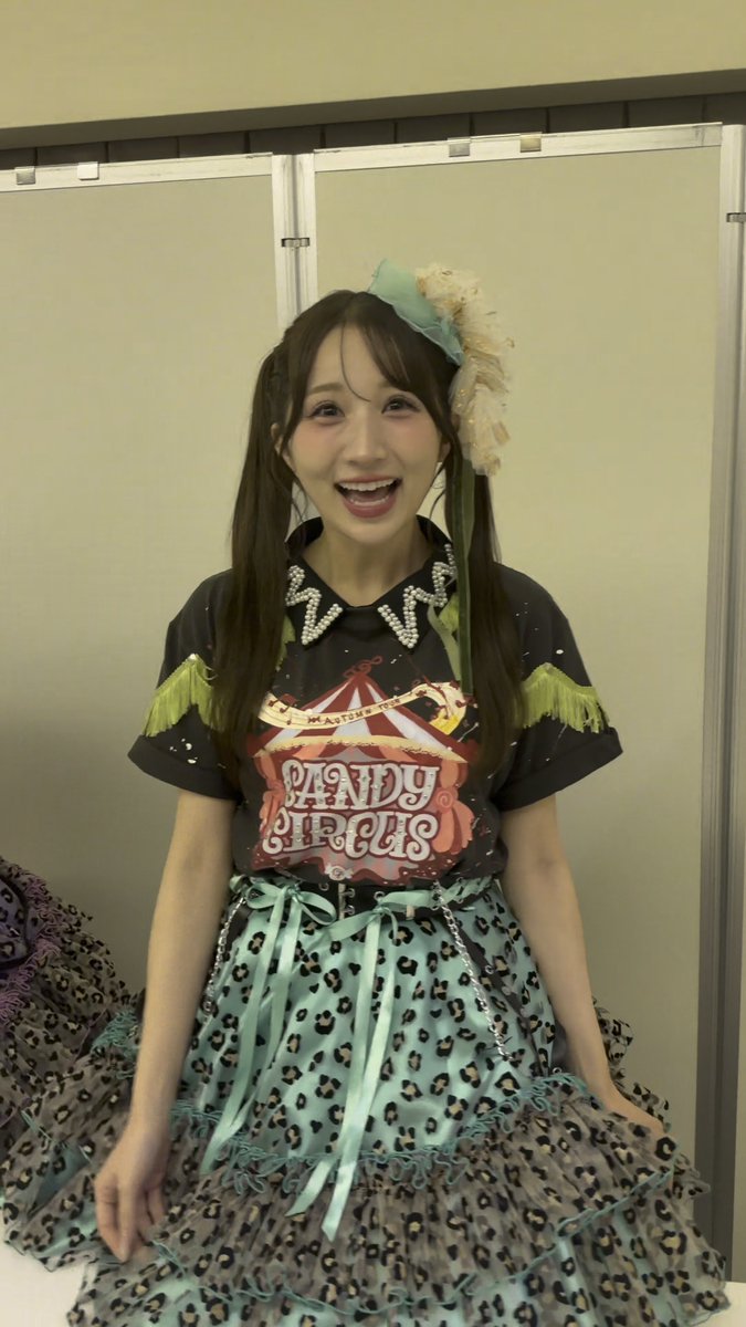 A woman wearing a colorful circus-themed outfit with a "CANDY CIRCUS" graphic tee, turquoise leopard-print skirt, and matching hair accessories, smiling excitedly.