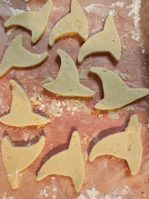 Raw witch hat-shaped cookies or pastry cutouts arranged on a floured baking surface.
