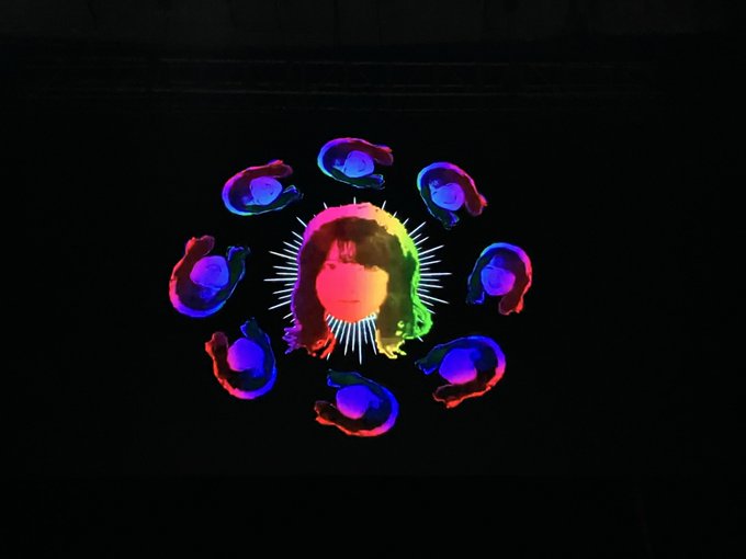 A stylized graphic shows a central face surrounded by eight silhouetted figures in vibrant rainbow colors against a black background.