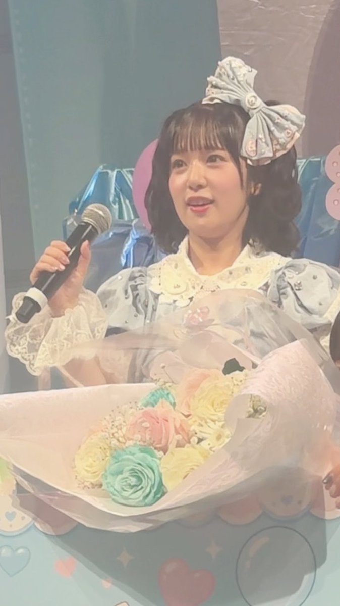 A woman holding a microphone and a bouquet of pastel-colored roses, wearing a light blue dress with a large bow headband.