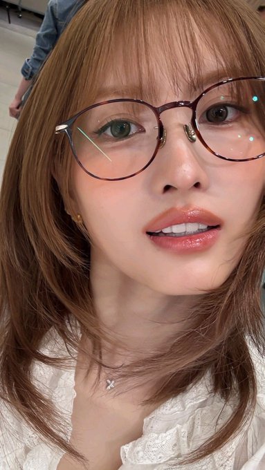Close-up selfie of a woman wearing round purple glasses and a white top.