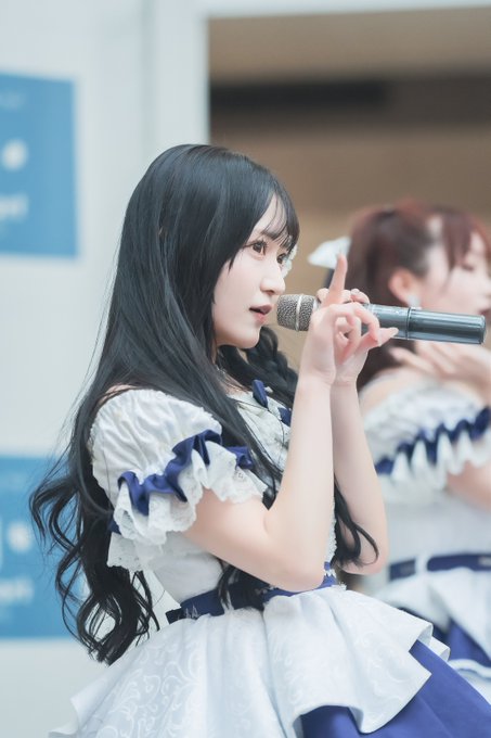 A performer with long dark hair in a white and blue dress holds a microphone on stage.